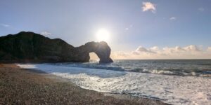 Shot of limestone arch Durdle Door from the beach with the sun just appearing above the arch.