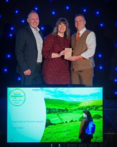 Foot Trails Founders standing on a stage receiving the Bronze Award in International Tourism.