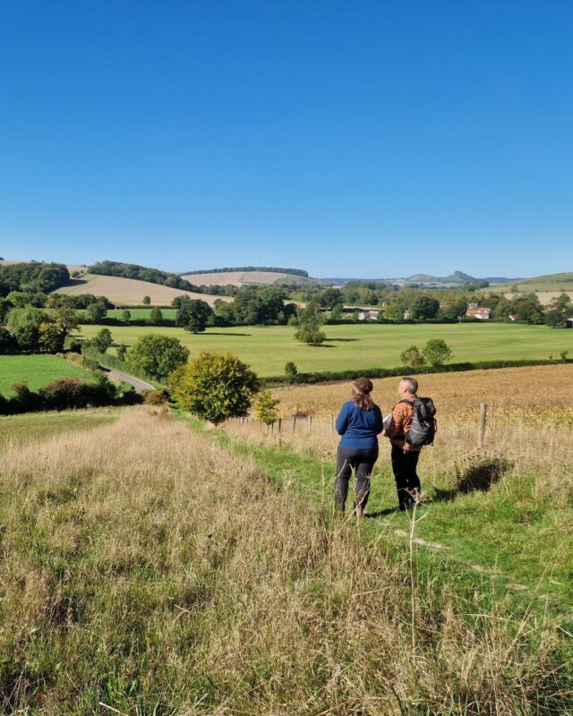 Two walkers are standing in a field with a map in hand. They are both looking out into the countryside in front of them