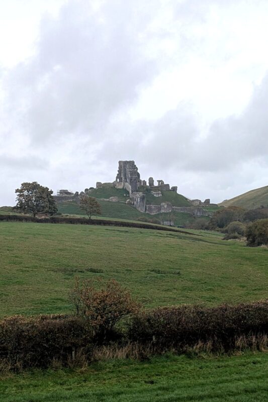 A dramatic ruined castle sits on top of a hill surrounded by countryside