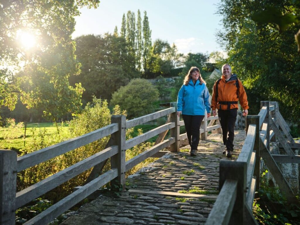 Two walkers cross an ancient cobblestone bridge