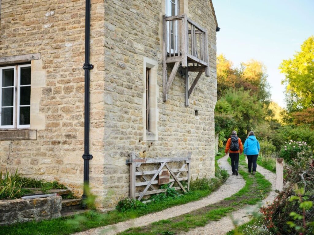 Two people walk off into the distance on a track past a traditional stone house.
