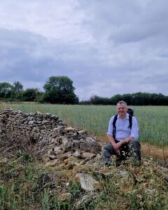 Foot Trails Co-Founder David Howell sitting on a wall in a field.