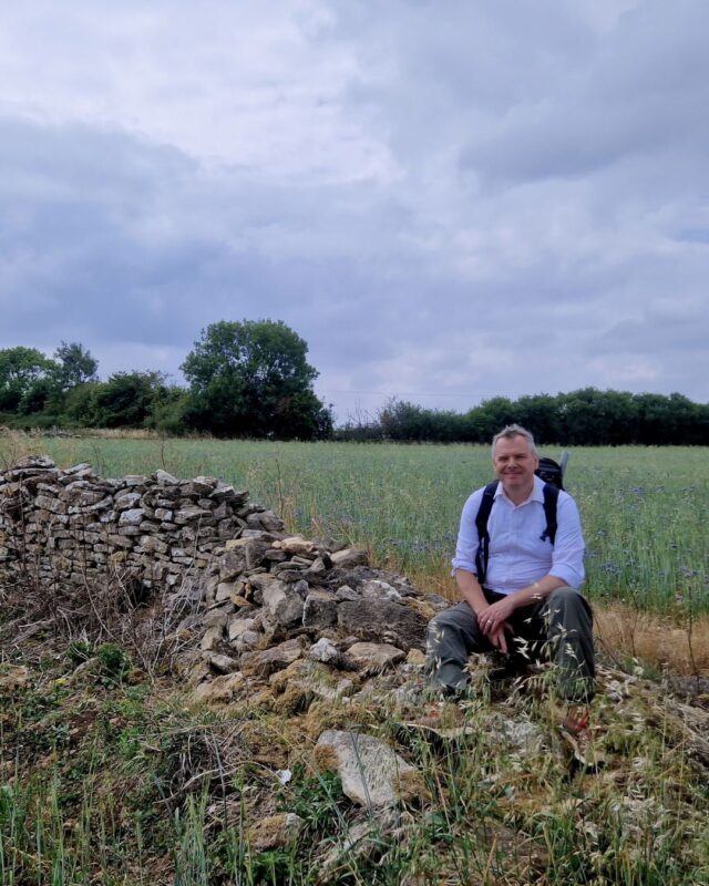 Foot Trails Co-Founder David Howell sitting on a wall in a field.