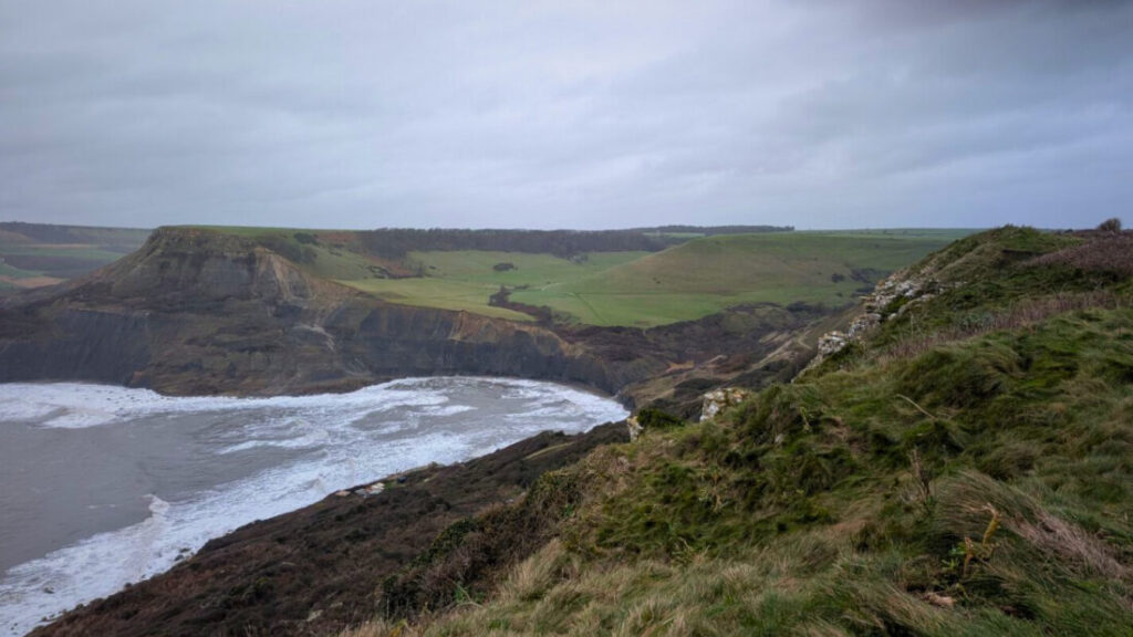 A wintery view of the Dorset coast, with cliffs and rolling green countryside stretching off into the distance and a white frothy sea to the left.
