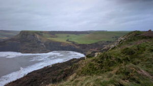 A wintery view of the Dorset coast, with cliffs and rolling green countryside stretching off into the distance and a white frothy sea to the left.