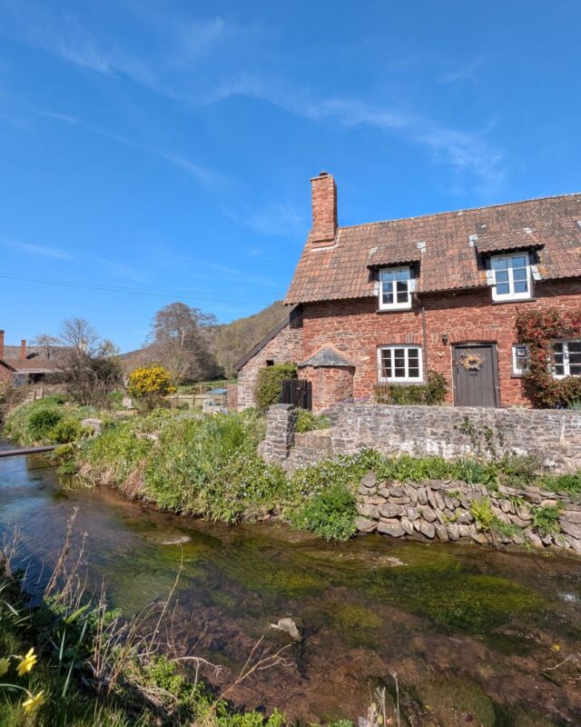 A red brick cottage next to a stream.