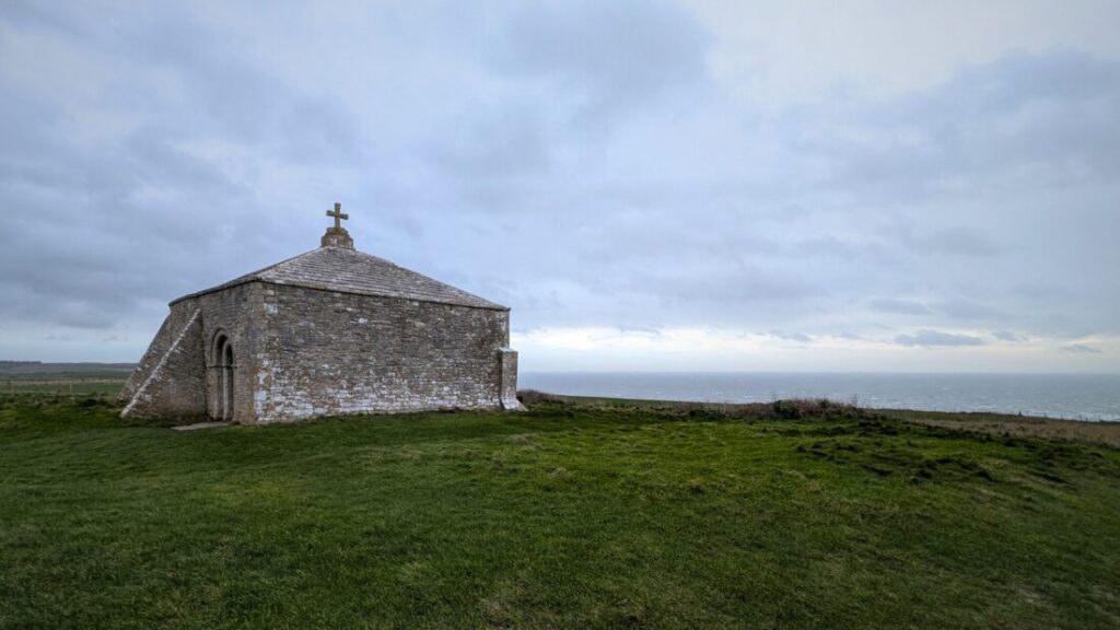 An old stone chapel sits on top of a cliff looking out to sea.