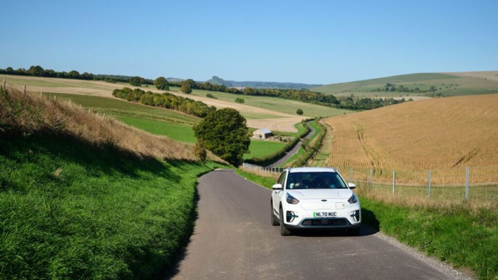 A white car on a quiet country lane surrounded by beautiful rolling countryside.