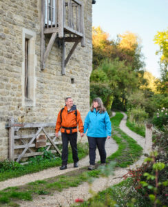 Hiking in The Cotswolds, England Two people walking down a gravel path in front of a stone cottage