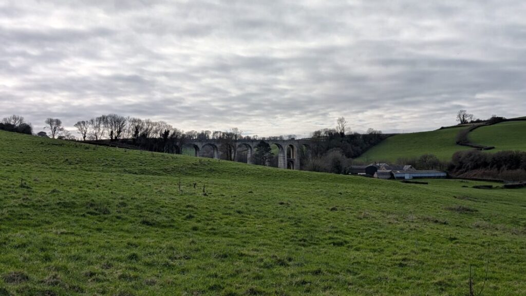View across a green field with an old stone viaduct int he distance.