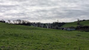 View across a green field with an old stone viaduct int he distance.
