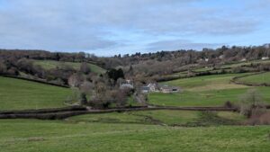 View over a green rolling landscape in winter with a village nestled in the distance.