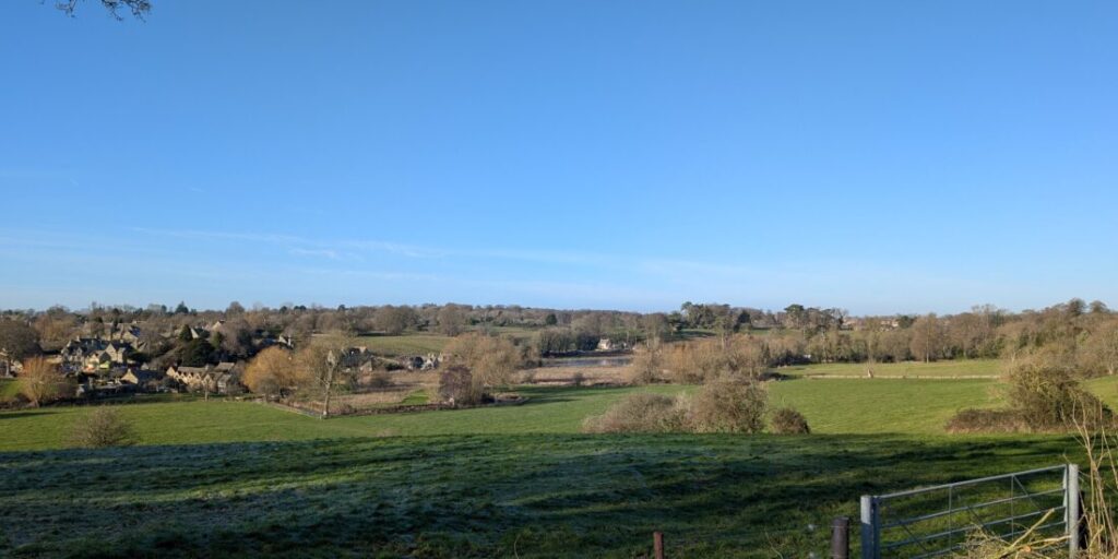 View over rolling Cotswolds landscape with a village in the distance.