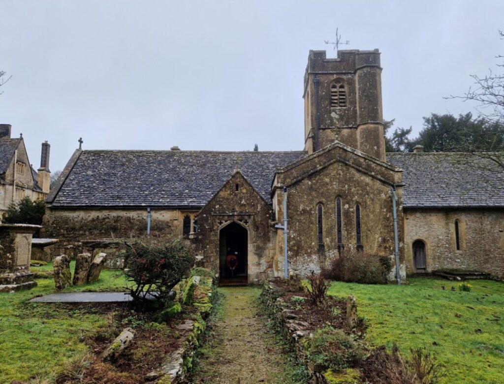 A gravel path leading up to a Norman church in the Cotswolds under a grey February sky