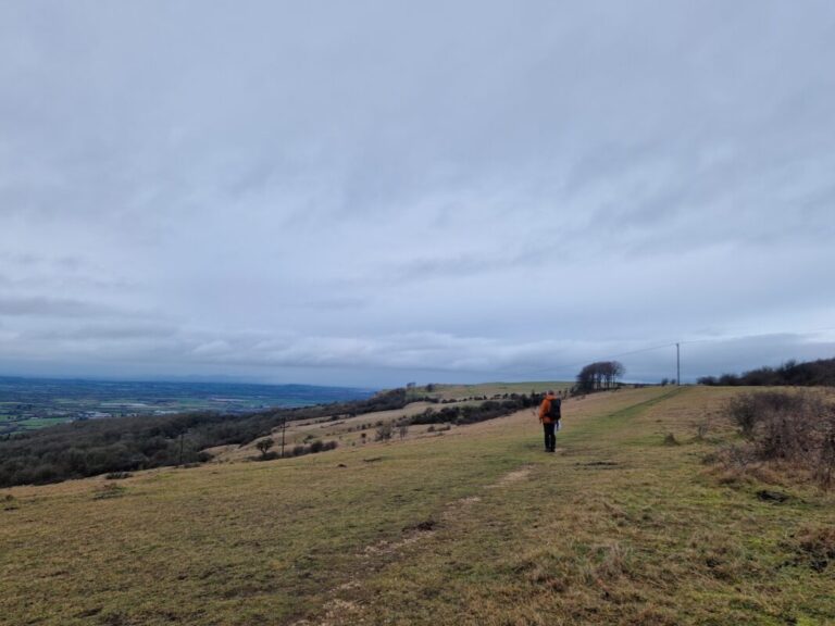 A lone walker stands on the edge of a hill looking out at the view on a winter's day.