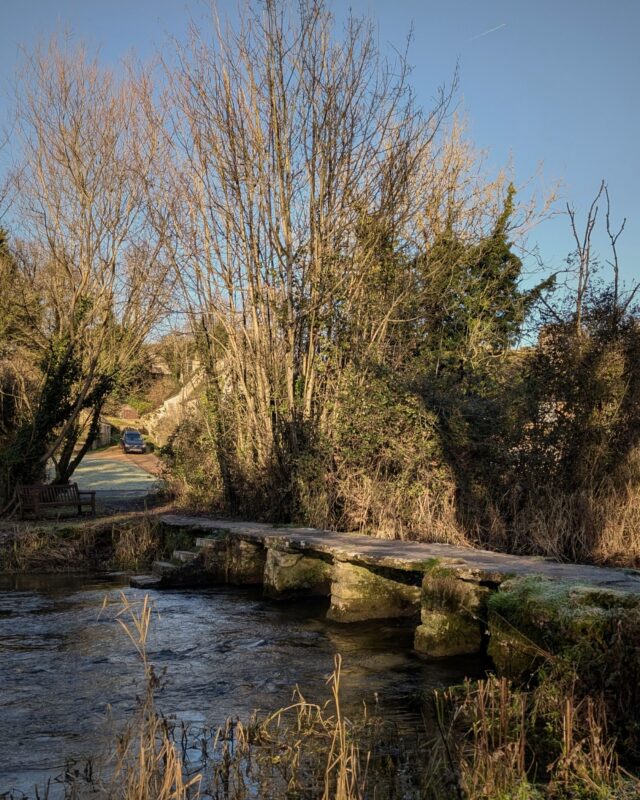 An ancient clapper bridge in the Cotswolds spanning a river on a bright winter's day.