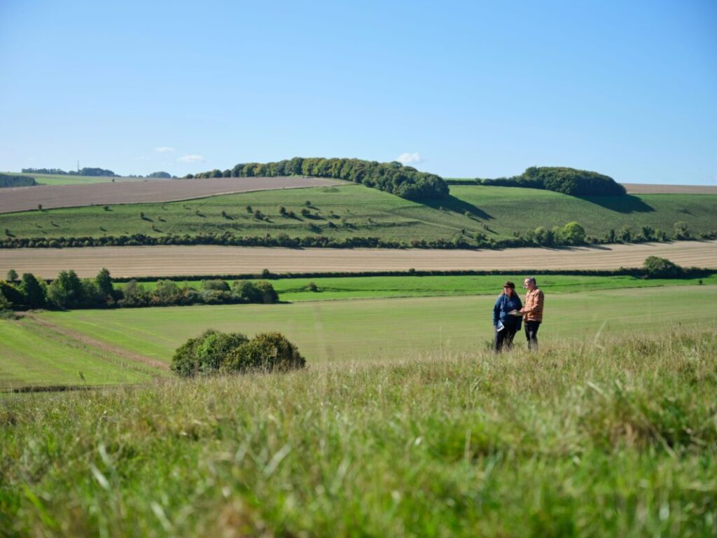 Two walkers stood in rolling green countryside looking at a map.