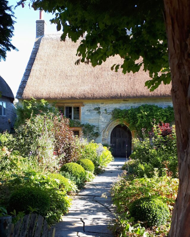 View of a path through a traditional English country garden leading to a thatched cottage.