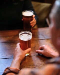 Two people sat at a wooden table with two pints of beer.