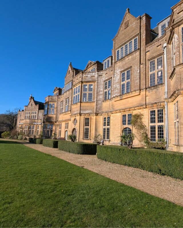 View of a grand country house with a footpath and lawn in front of it.