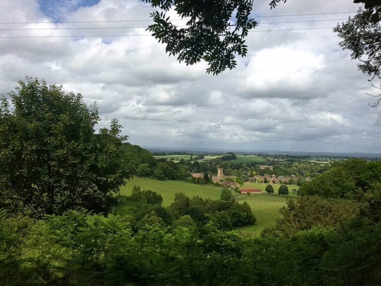 View of rolling green landscape with a pretty stone village nestled between the hills and trees.