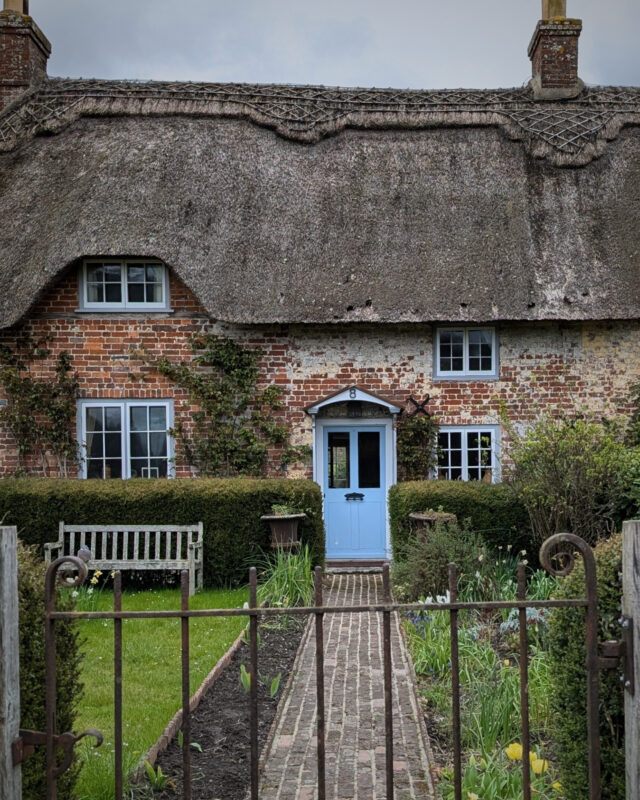 View of a footpath leading up to the front door of a thatched stone cottage.