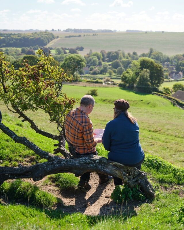 David and Alison Howell sit on bent over tree trunk looking at a map.