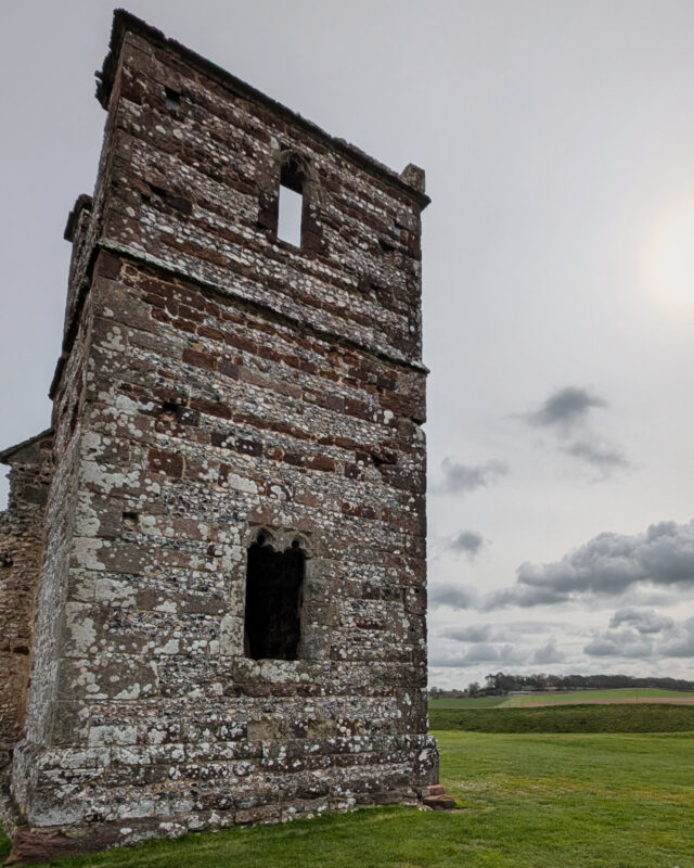 The tower of a ruined church looms over a green field.