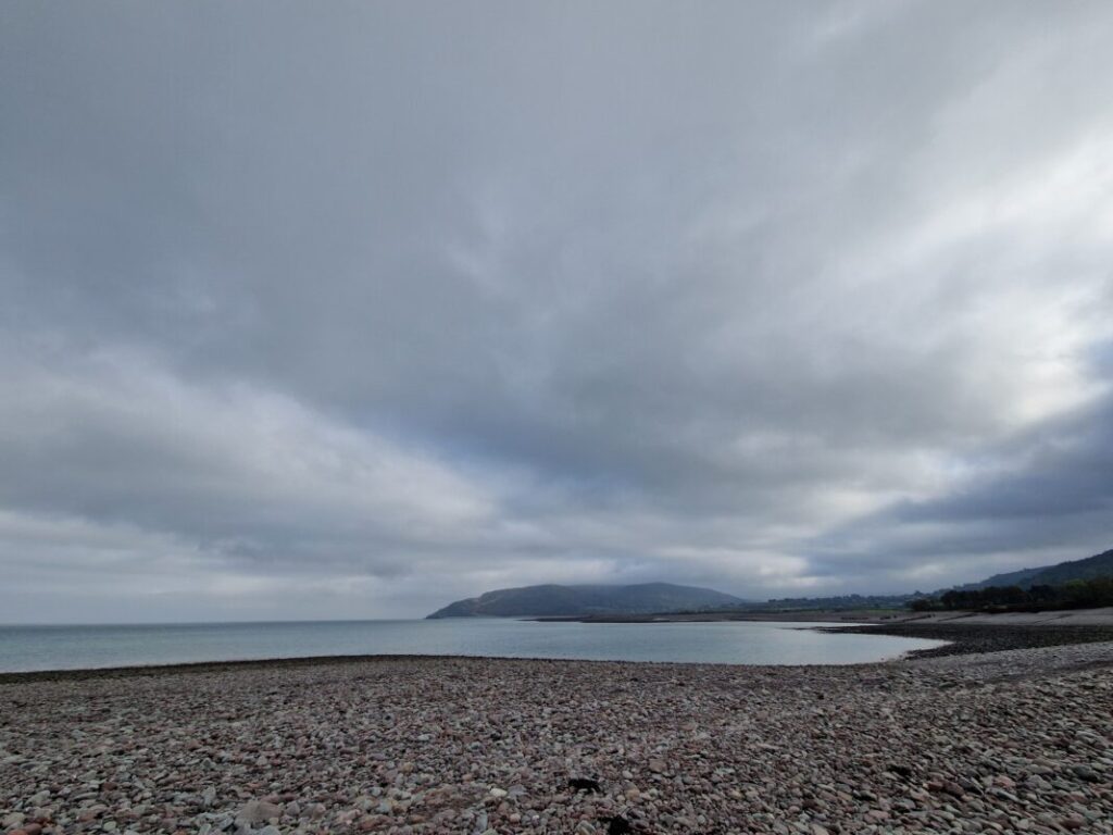 View of a blue-grey sea from a pebble beach with a cove and cliffs to the right
