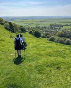 A group of hikers walk downhill towards rolling green landscape on a sunny day