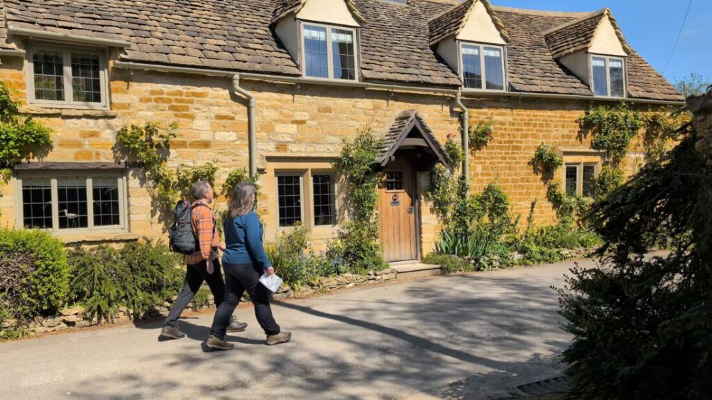 Foot Trails Founders Alison & David Howell walking in front of a row of classic Cotswolds cottages.