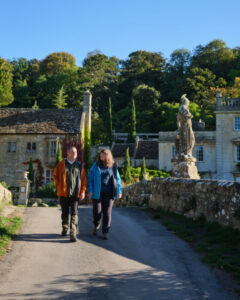 Two hikers are walking over an ornate stone bridge in front of a beautiful country mansion.