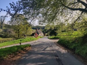 View of a quiet country lane with a red telephone box and cottage in the distance.
