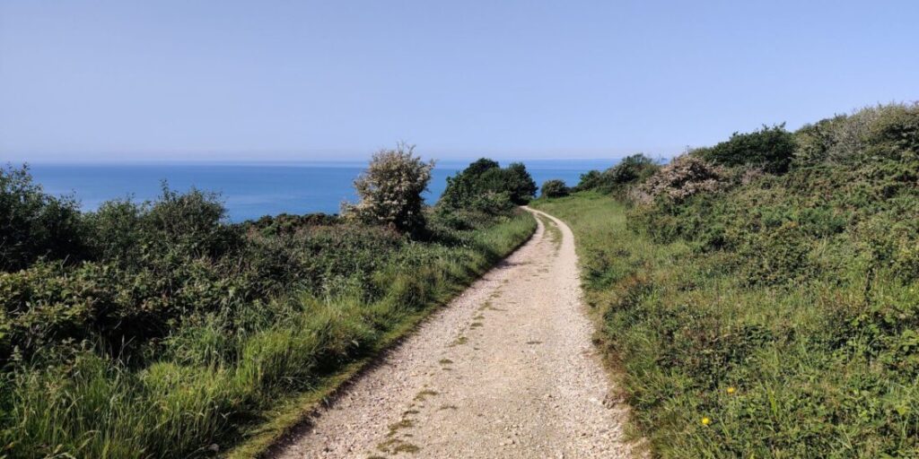 View of a gravel track stretching off into the distance with the blue sea shimmering in the background.