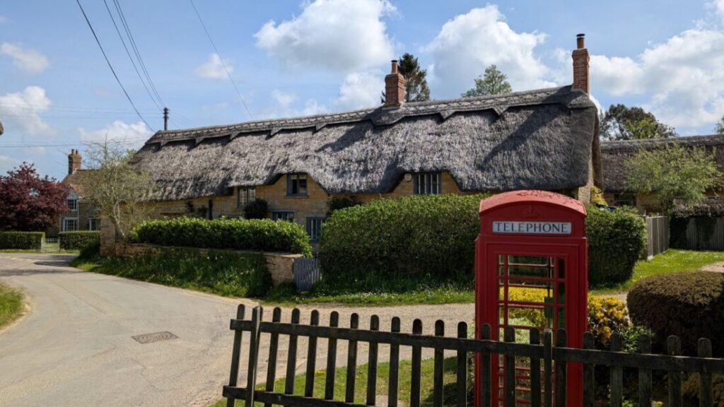 A long thatched cottage in a village with a red telephone box in front of it