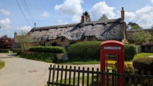 A long thatched cottage in a village with a red telephone box in front of it