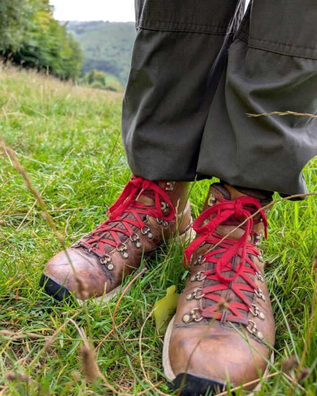Close up of a hiker's legs, wearing dark green hiking trousers and leather hiking boots