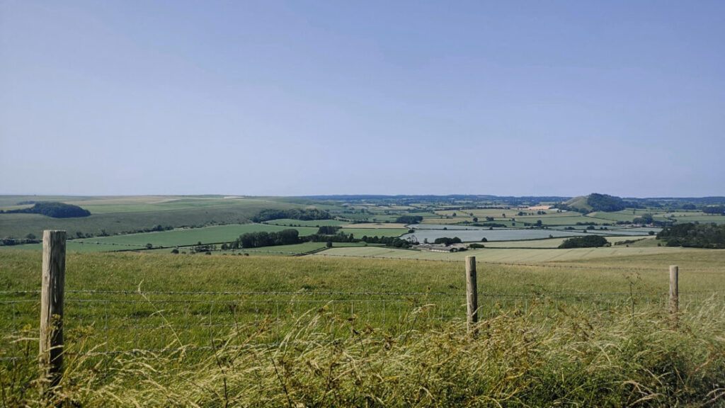 View from the top of a hill over a patchwork of rolling green fields.