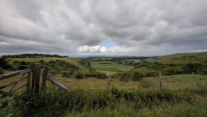 View over a valley of patchwork farm fields nestled between green hills with a wooden gate to the right