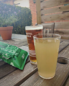 Photo of a pint of beer, a soft drink and a packet of drinks on a table in a beer garden.