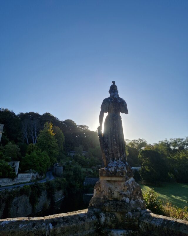 A stone statue on a bridge silhouetted against the morning sun.