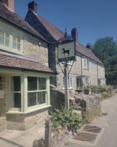 The outside of an stone old country inn with a sign showing a black dog.