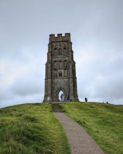 View of the church tower on Glastonbury Tor with the footpath leading to the tower and some people looking at the tower.