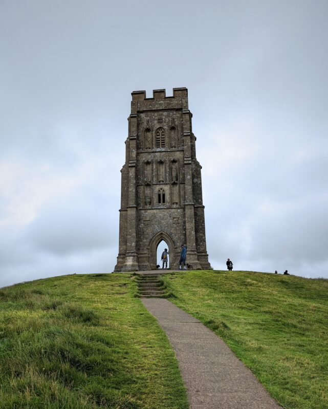 View of the church tower on Glastonbury Tor with the footpath leading to the tower and some people looking at the tower.
