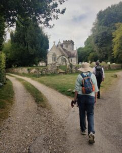 Two hikers walking along a gravel path towards a church surrounded by trees.