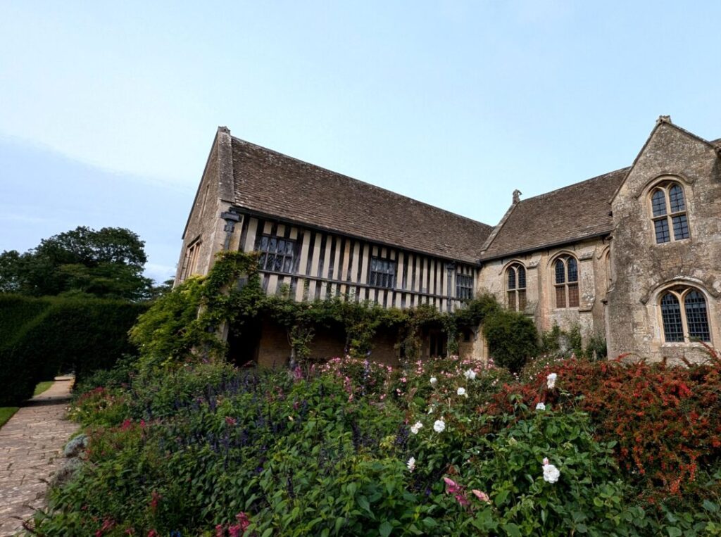 An old country house with a timber frame exterior with gardens in front.
