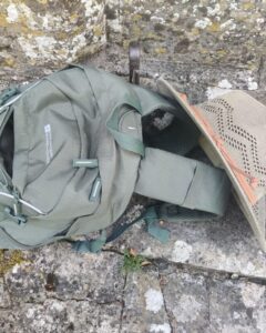 Photo of a hiking rucksack on the ground with a sun hat leaning against it.