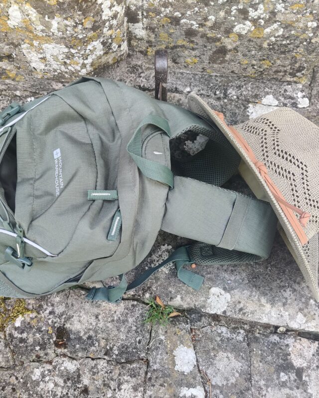 Photo of a hiking rucksack on the ground with a sun hat leaning against it.