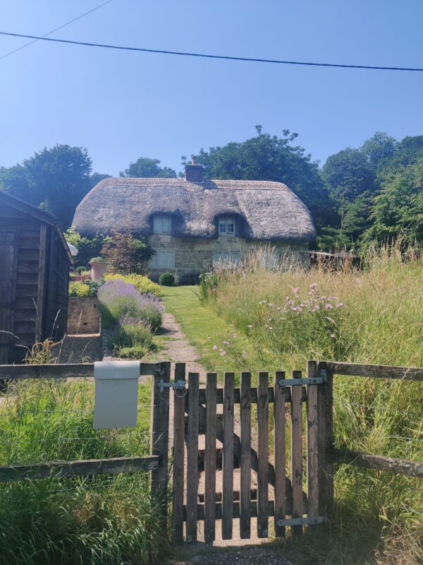 A wooden gate leading up a garden path to a traditional thatched cottage.